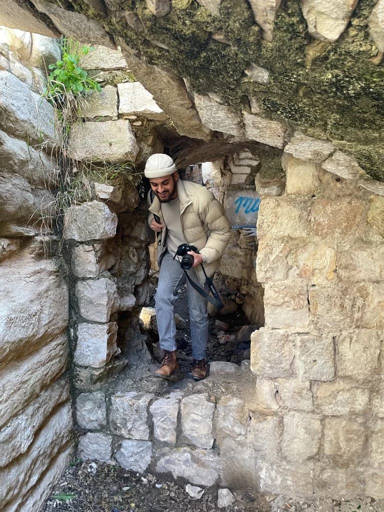 A photographer carrying a camera steps through a weathered stone opening
